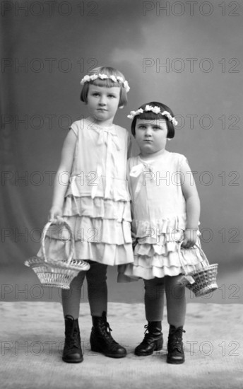2 girls with wreaths of flowers, 1910, Two girls in dresses with baskets of flowers pose in a