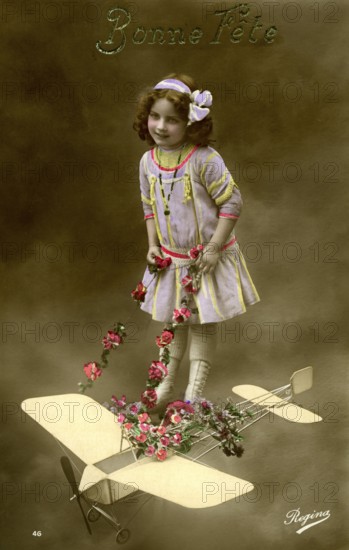 Girl with aeroplane, 1910, Girl in a purple dress posing with a toy aeroplane and flowers,