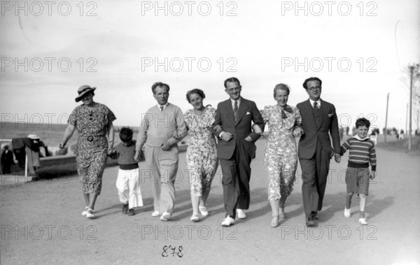 Family outing on the beach promenade, 1930s, A group of people stroll along the beach in elegant