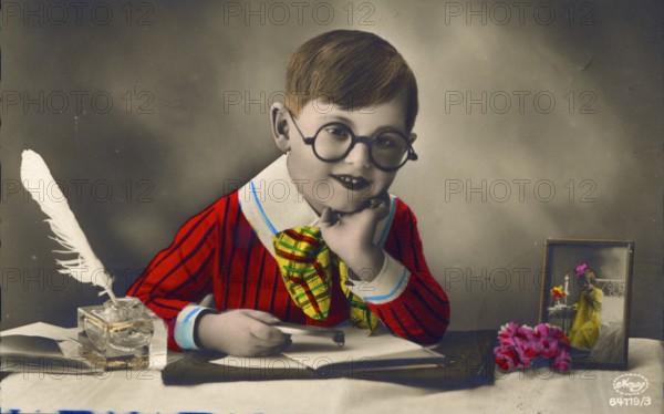 Little boy with colourful clothes sitting at desk and writing love letter, 1920s, Child with