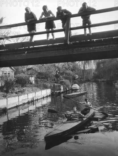 Four children on a bridge, 1930s, Children standing on a bridge while teenagers paddle underneath