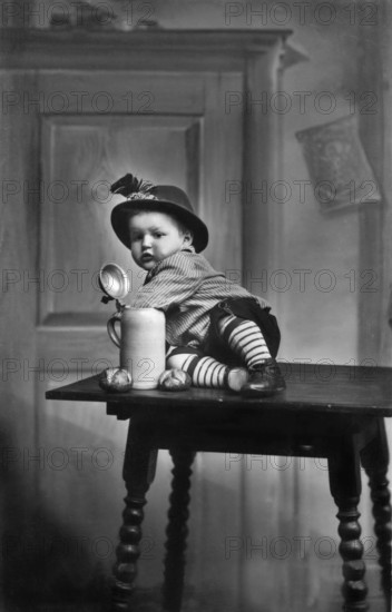 Baby traditional traditional costume beer mug, 1930s, child in traditional dress sitting on a table