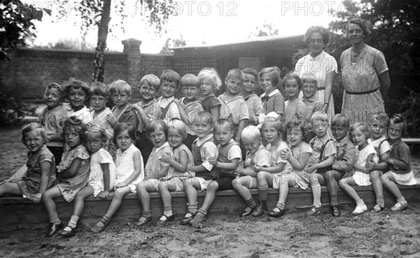 Kindergarten, 1920s, group of children and two woman outdoors, cheerful atmosphere, black and