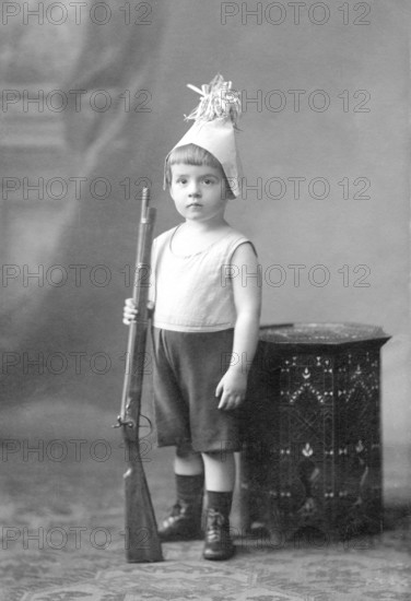 Little boy rifle, 1910s, boy in costume with toy rifle, serious face, vintage studio shot,