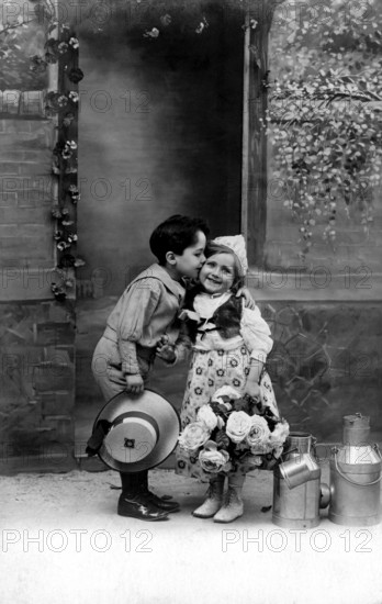 Boy kisses girl, 1920s, A boy kisses a girl on the cheek, surrounded by flowers and pewter cans,