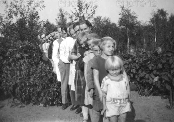 Standing in line, 1920s, family posing in a row in the garden, surrounded by plants, historical