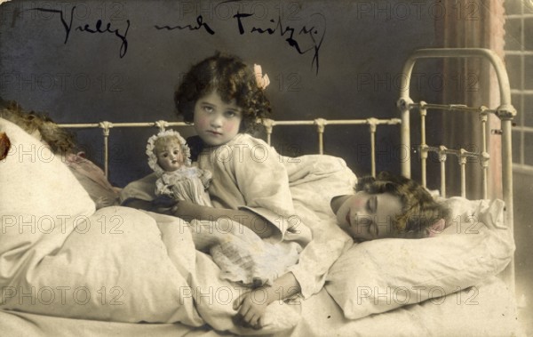 Two girls in bed, 1920s, Two children in bed, one awake with doll, the other asleep, atmospheric,