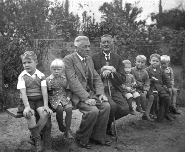 Short and tall men, 1920s, grandfather and children on an outdoor bench, symbolises family ties