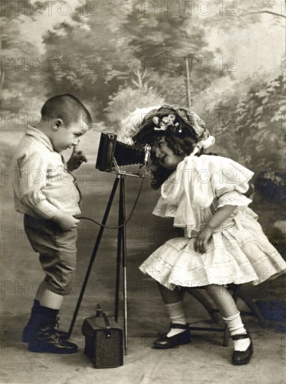 Children's camera self-timer 1906, Two children playing with an old camera, one looking at the