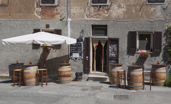 Enoteca with wooden barrels as tables and bar stools under a large parasol in front of an old house