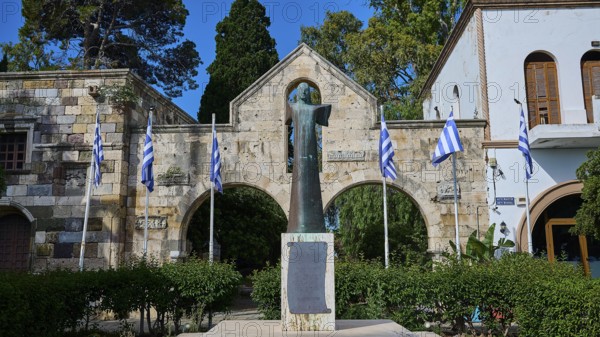 Statue surrounded by Greek flags and historical architecture in the garden, Kos Town, Venetian City