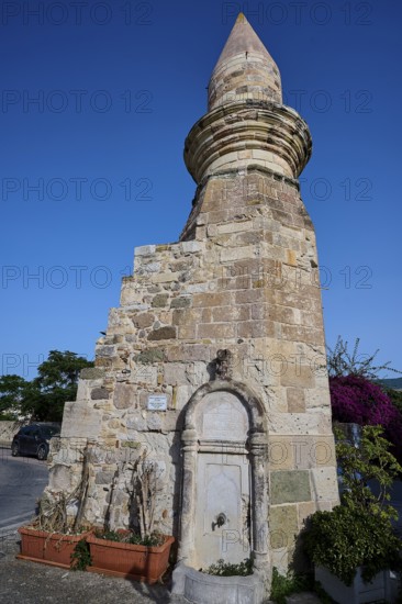 Historic fountain next to a stone tower under a clear blue sky, Eski Cami, Minaret, Kos Town, Kos,
