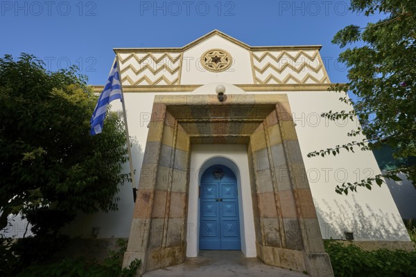 Greek architecture with turquoise door and flag on bright, sunny background, Synagogue, Kos Town,