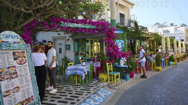 Guests sitting outside in front of a tavern decorated with flowers in kos, friendly atmosphere,