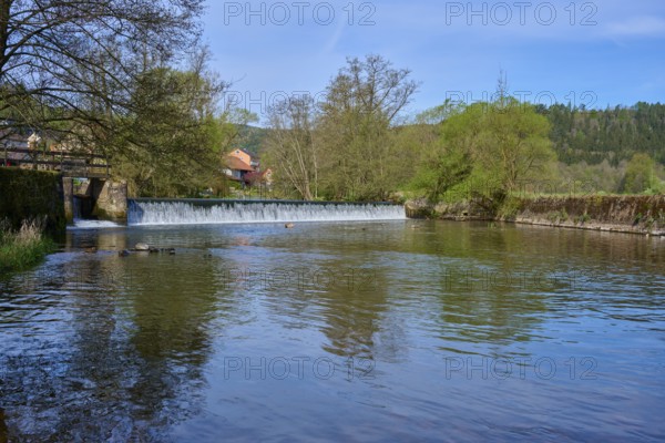 Calm river water in front of a dam wall, surrounded by green nature and blue sky, spring, Obersinn,