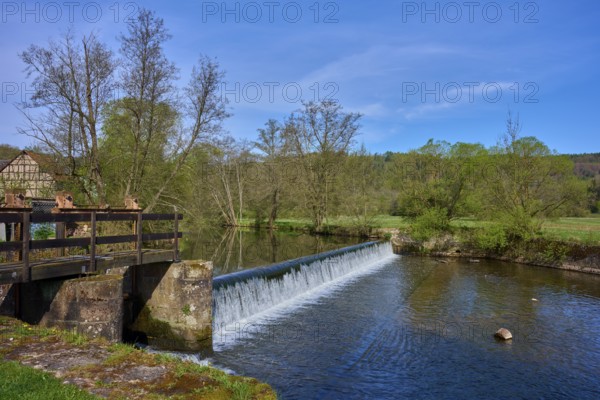 A weir in the river leads to a small waterfall, surrounded by trees, spring, Obersinn, Sinntal,