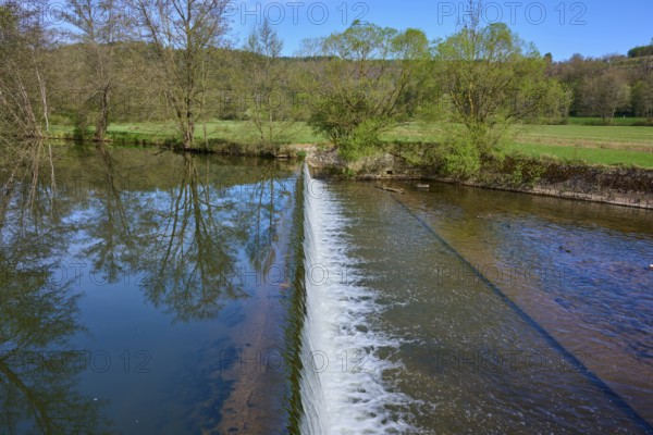 Small dam wall with falling water and reflection of the trees in the river, spring, Obersinn,
