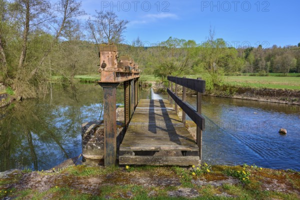 Wooden footbridge over a body of water in a natural setting with trees in the background, spring,