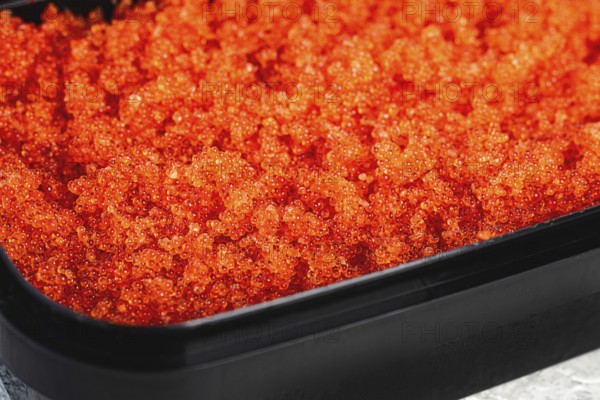 Container with orange caviar, flying fish, Tobiko, on the table, caviar for rolls and sushi,