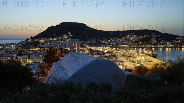 Chapel Agia Paraskevi, town with harbour at dusk, illuminated, hill in the background, Skala,