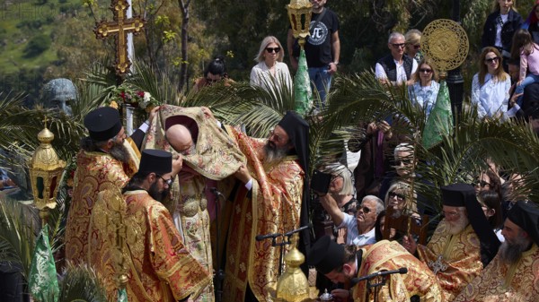 Priests standing under a cross during an outdoor religious ceremony surrounded by worshippers and