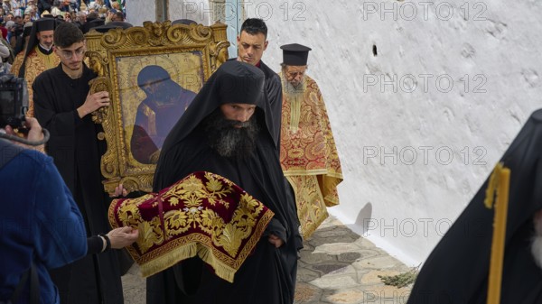 A priest in a black robe leads a procession while another carries an icon, Orthodox ceremony, monks