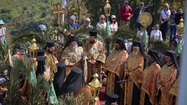 Clergy in richly decorated robes at an open-air ceremony, surrounded by palm trees and spectators,