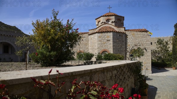 Stone church with tiled roof, surrounded by a blooming garden under a blue sky, woman's monastery,