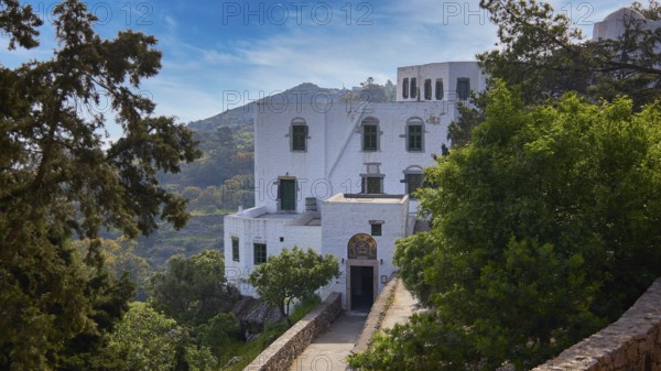 White monastery building surrounded by dense vegetation and a sunny sky, Monastery of the