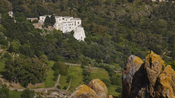 White building from a distance in a wooded landscape with rocks in the foreground, Monastery of the
