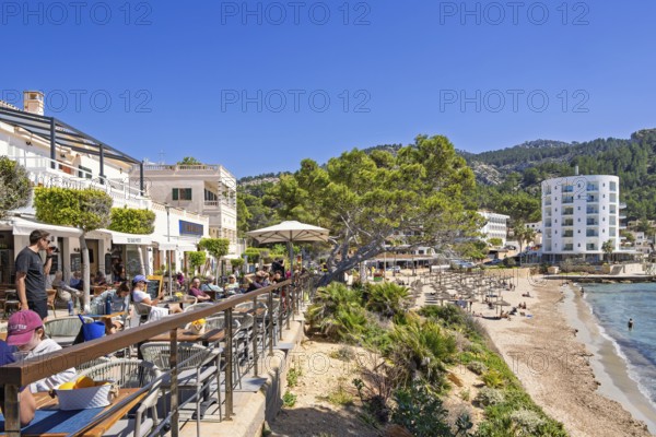 Outdoors restaurant on a terrace with tourist sitting in the sunshine and looking at the seascape