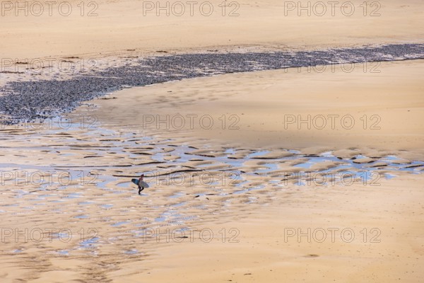 Man with a surfboard walking on a sand beach on the way to the sea a sunny summer day, Crozon