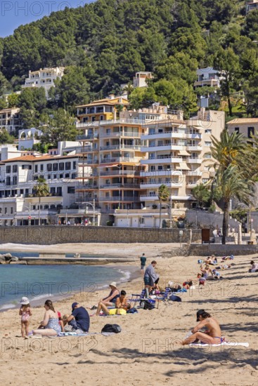 People sunbathing on a sandy beach at a tourist resort with houses close to the shore at the