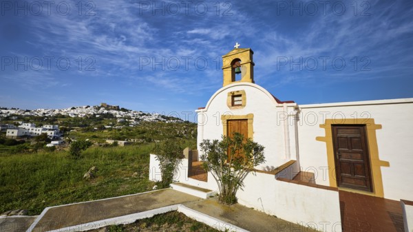 White chapel with wooden door and cross, surrounded by green nature, chapel south of the Chora,