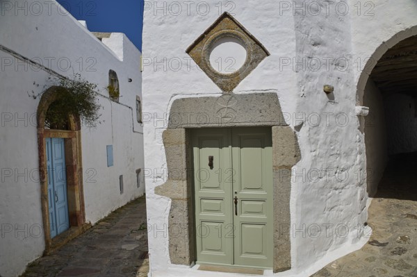 Green door with geometric frame in a white historic building with plants, Mantomata stones, Chora,