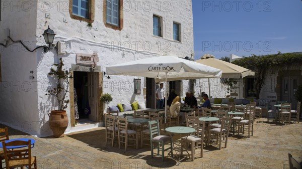 Cosy café terrace with parasols and rustic white buildings in the background, Platia Lesvias,