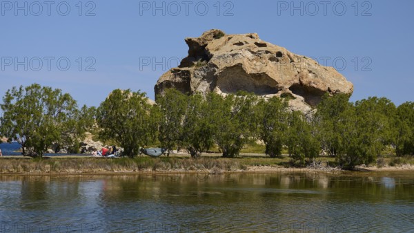 Rock rises behind a row of trees on the lakeshore under a clear sky, Rock of Kalikatsou, Seasonal