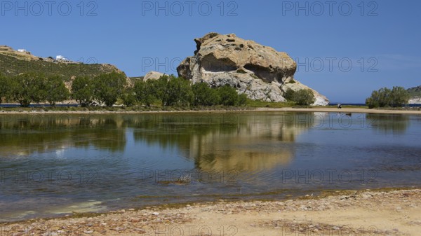 Large rock reflected in a calm lake under a blue sky, Rock of Kalikatsou, Seasonal Salt Lake,