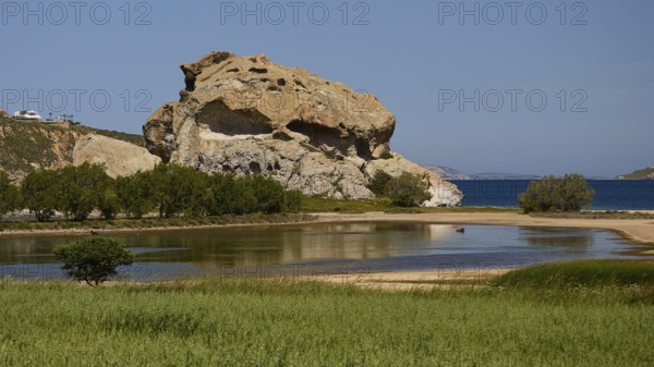 Dominant rock structure over an open water surface with green shore vegetation, Rock of Kalikatsou,