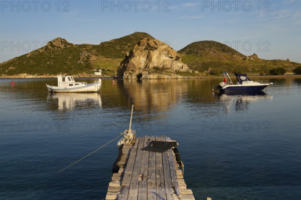 Two boats lying on calm water in front of rocky coastal landscape with wooden jetty in the