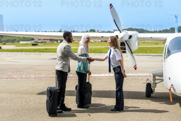 Female pilot greeting two passengers with a handshake next to a private airplane on the tarmac,
