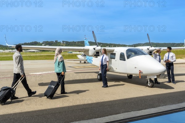 Passengers carrying trolley bags walking towards small airplane and flight crew, ready for boarding
