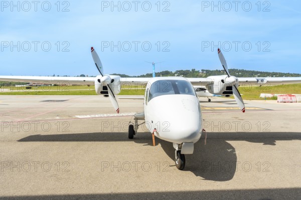 White twin engine turboprop airplane is parked on the tarmac of a small airport on a sunny day,