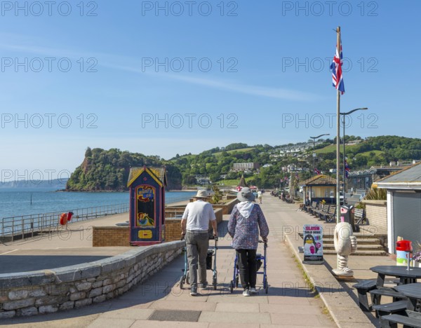Two elderly people walking with rollators, Seafront promenade view west towards Teignmouth, south