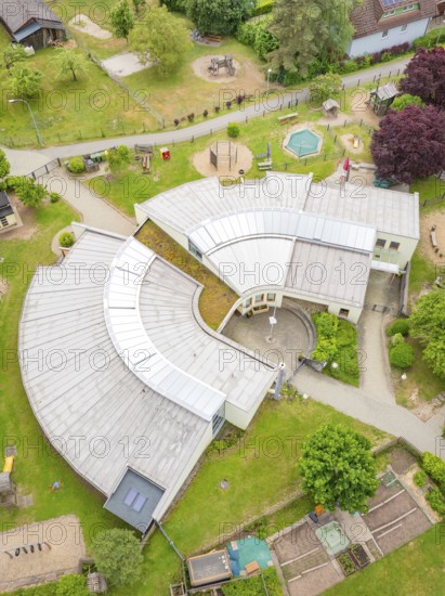 Modern architecture in a U-shaped building with surrounding greenery and playground facilities seen