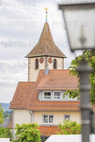Tower of a church with clock, surrounded by buildings with red roofs and a cloudy sky, family