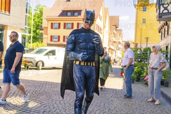 Man in Batman costume walking in a busy sunny city centre, Calw train station festival, Black