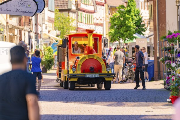 Tourist train travelling through busy city street in the sunshine, Calw station festival, Black