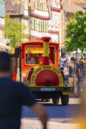 Colourful procession drives through a lively old town street, surrounded by passers-by, Calw