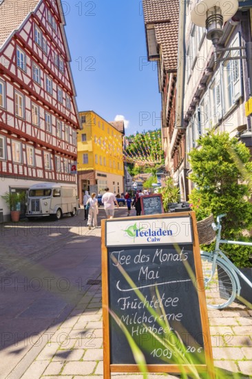 Half-timbered house street with board and bicycle in the foreground, sunny cityscape, Calw railway